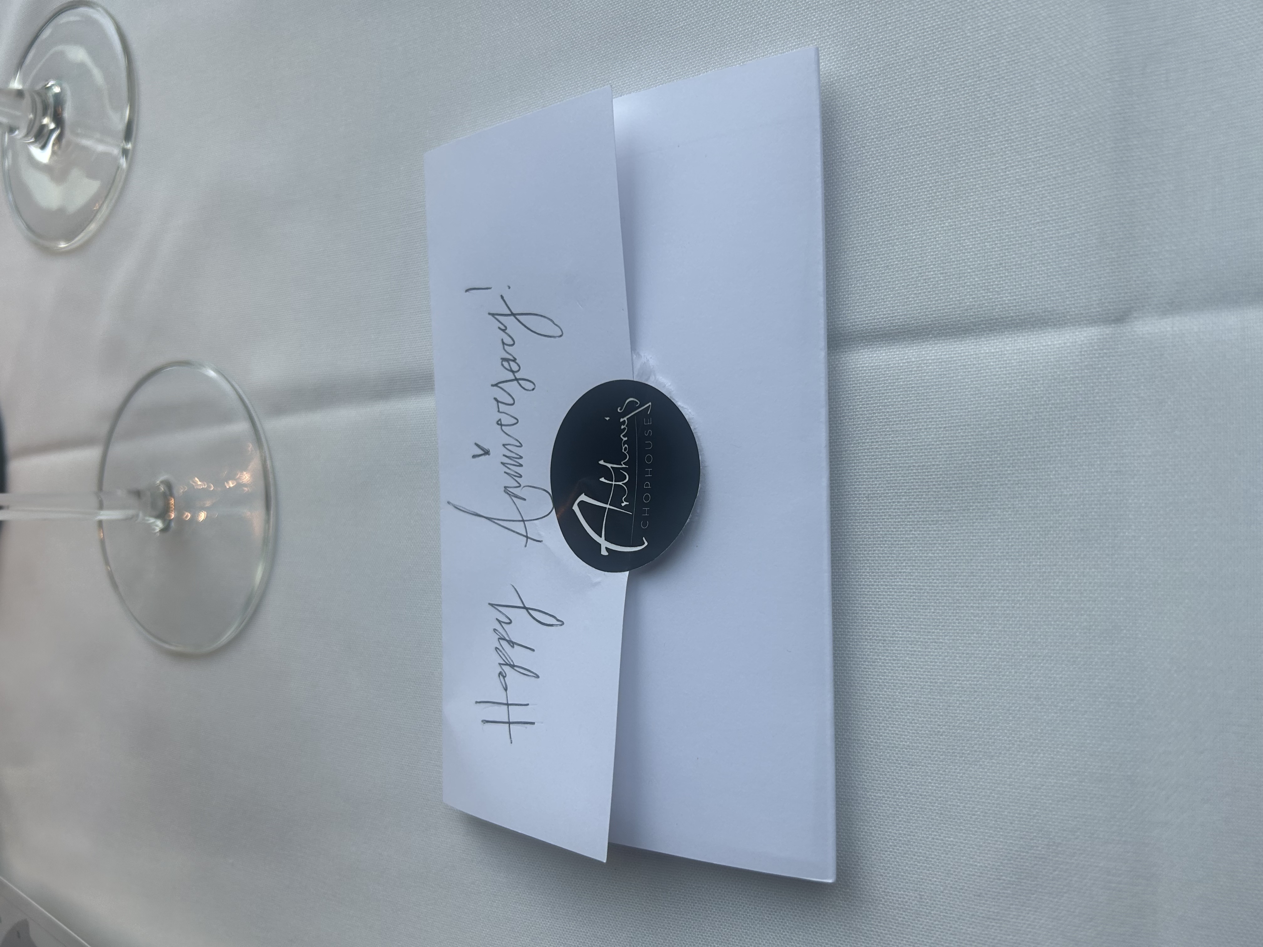 A handwritten Happy Anniversary card sealed with an Anthony's Chophouse sticker, waiting on the table