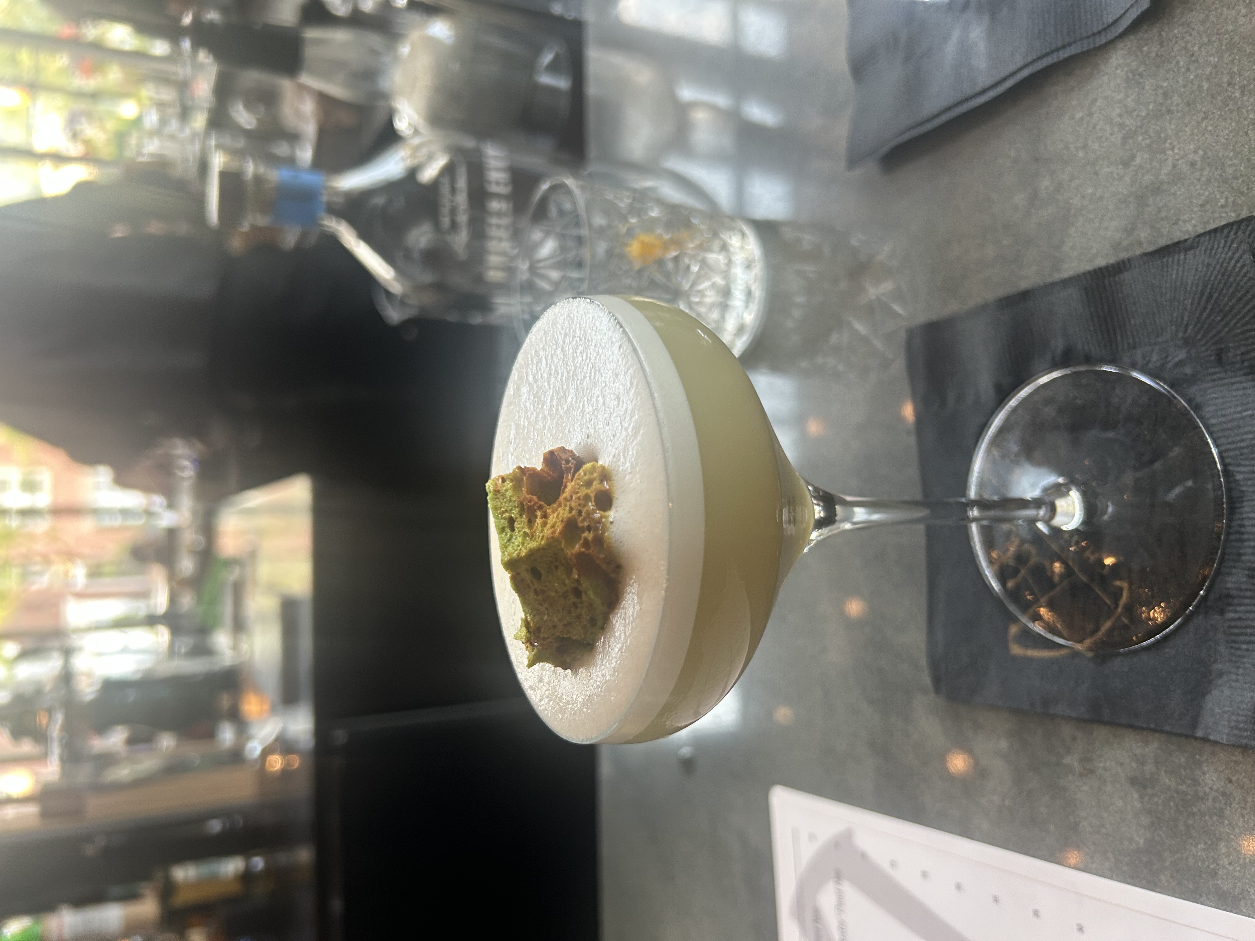 The Thank You Very Matcha cocktail in a coupe glass topped with foam and a piece of green honeycomb candy
